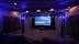 A cozy home theater room featuring soft lighting, plush seating, and a large projection screen with the Dreamedia logo.