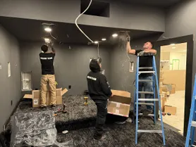 Workers from Dreamedia install lighting and wiring in a luxury home theater under construction, showcasing their teamwork.